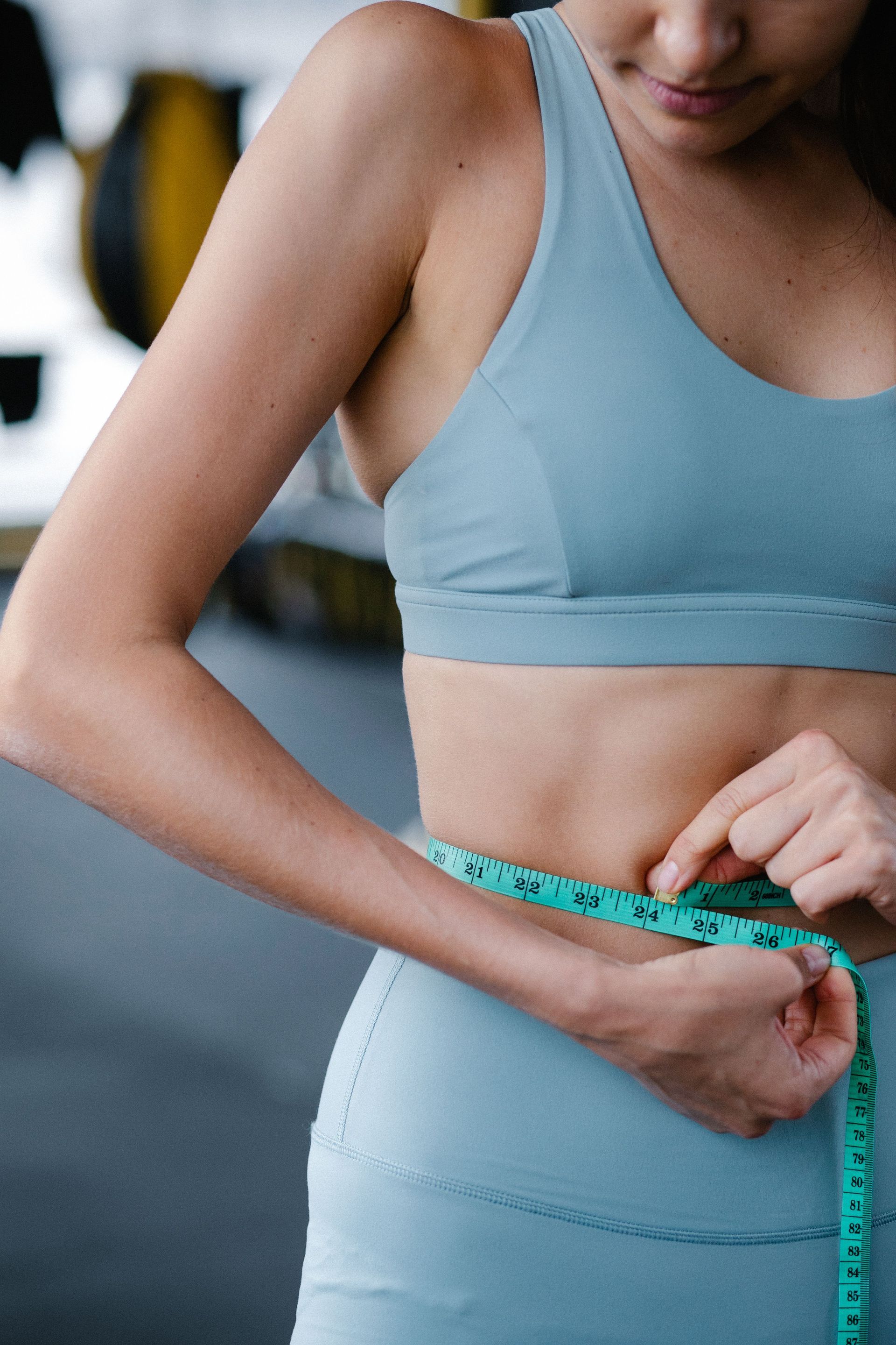 Person measuring waist with a tape measure in a gym, wearing blue athletic wear.