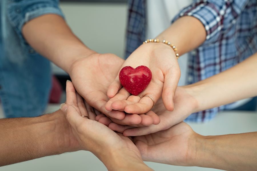 Several hands joined together while holding a heart, symbolizing support and care.