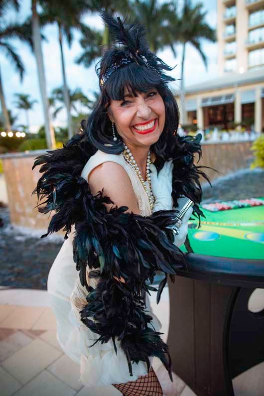 A woman in a white dress and black feather boa is standing next to a table.