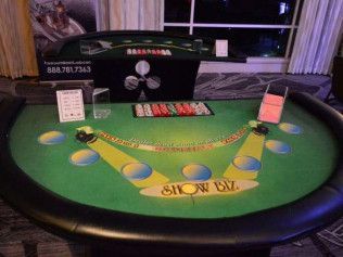 A poker table is sitting in a room next to a window.