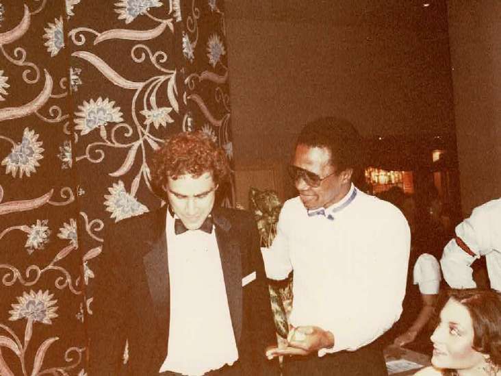 A man in a tuxedo is talking to another man