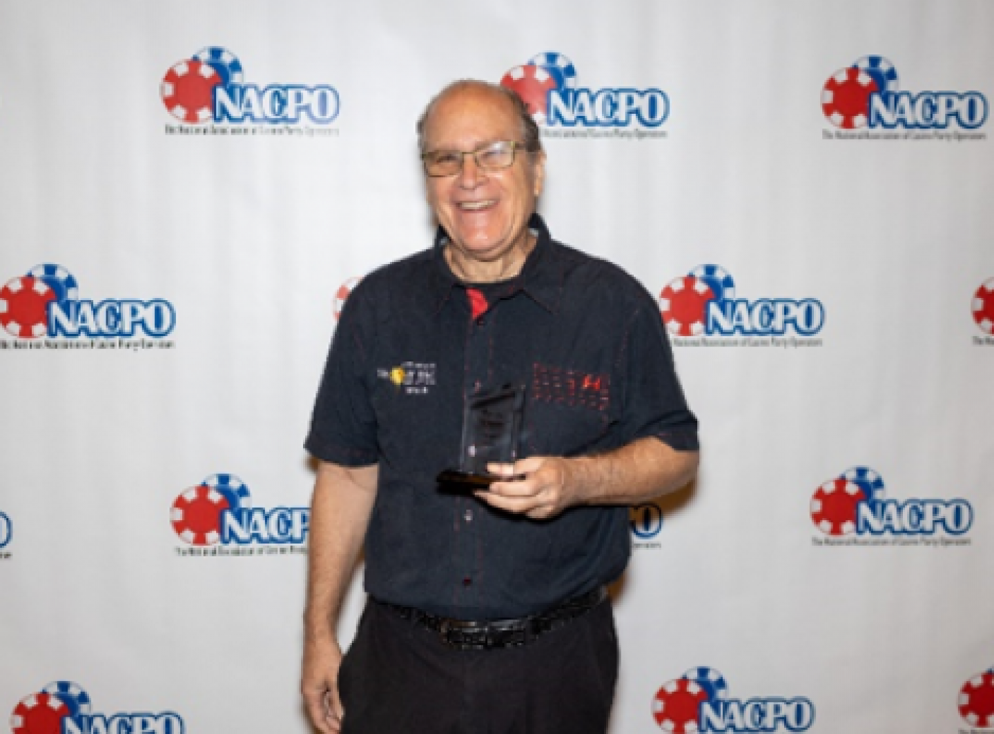 A man is holding an award in front of a backdrop that says nacho