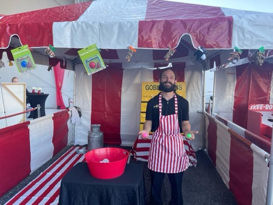 A man in a striped apron is standing in front of a carnival booth.