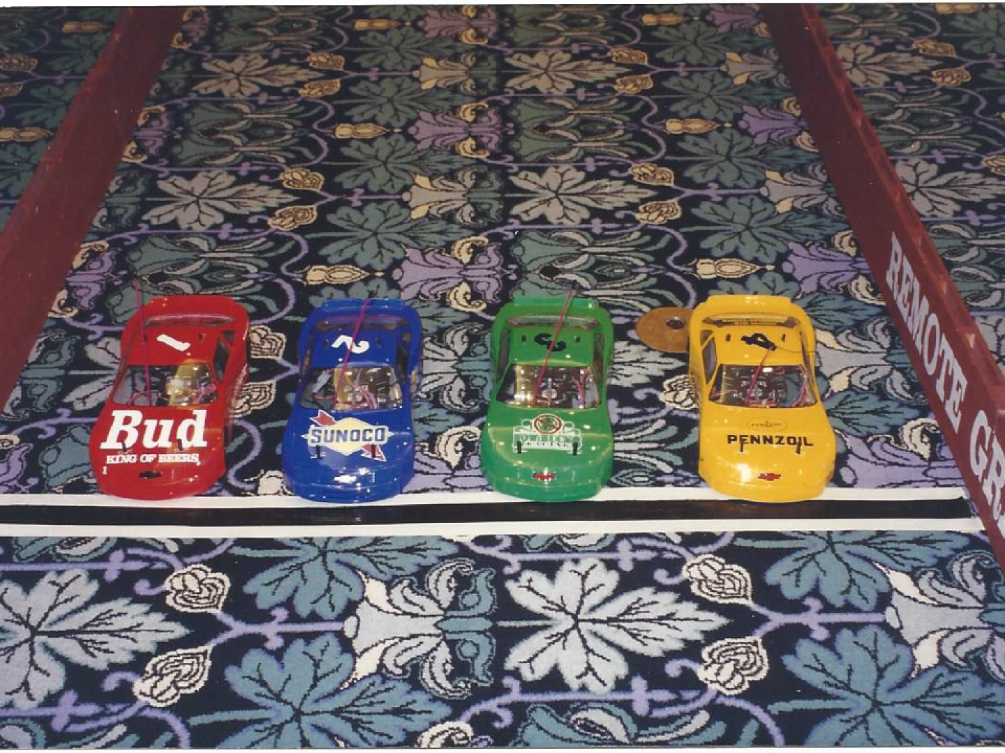 Four toy cars are lined up on a carpet and one of them says bud