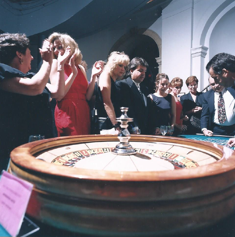 A group of people standing around a roulette wheel that says ' roulette ' on it