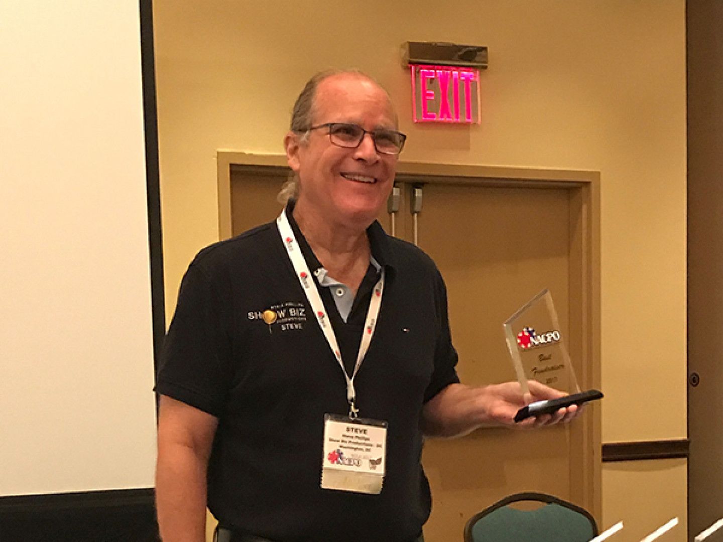 A man holding a trophy in front of an exit sign