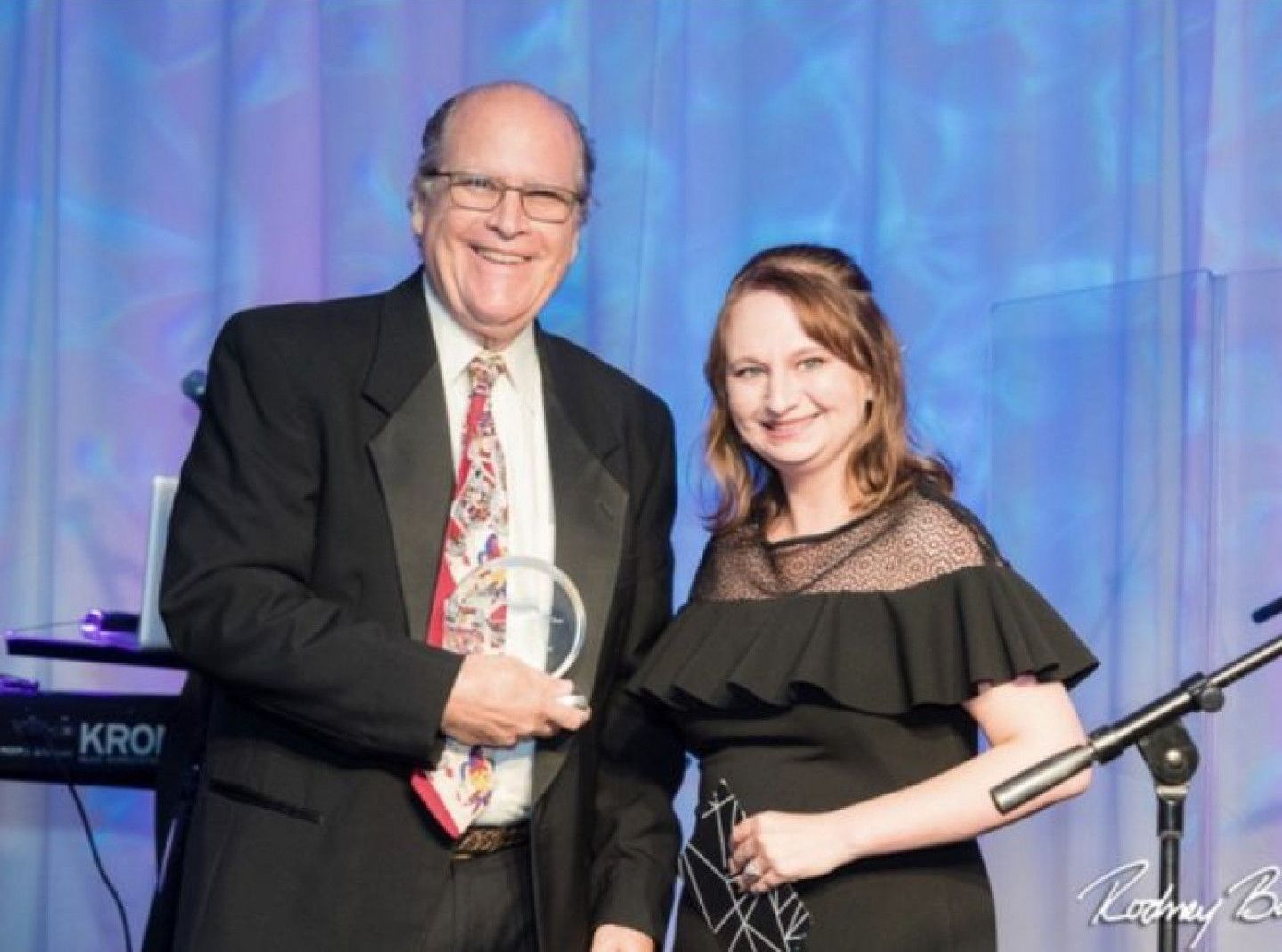 A man in a suit and tie is holding an award next to a woman in a black dress.