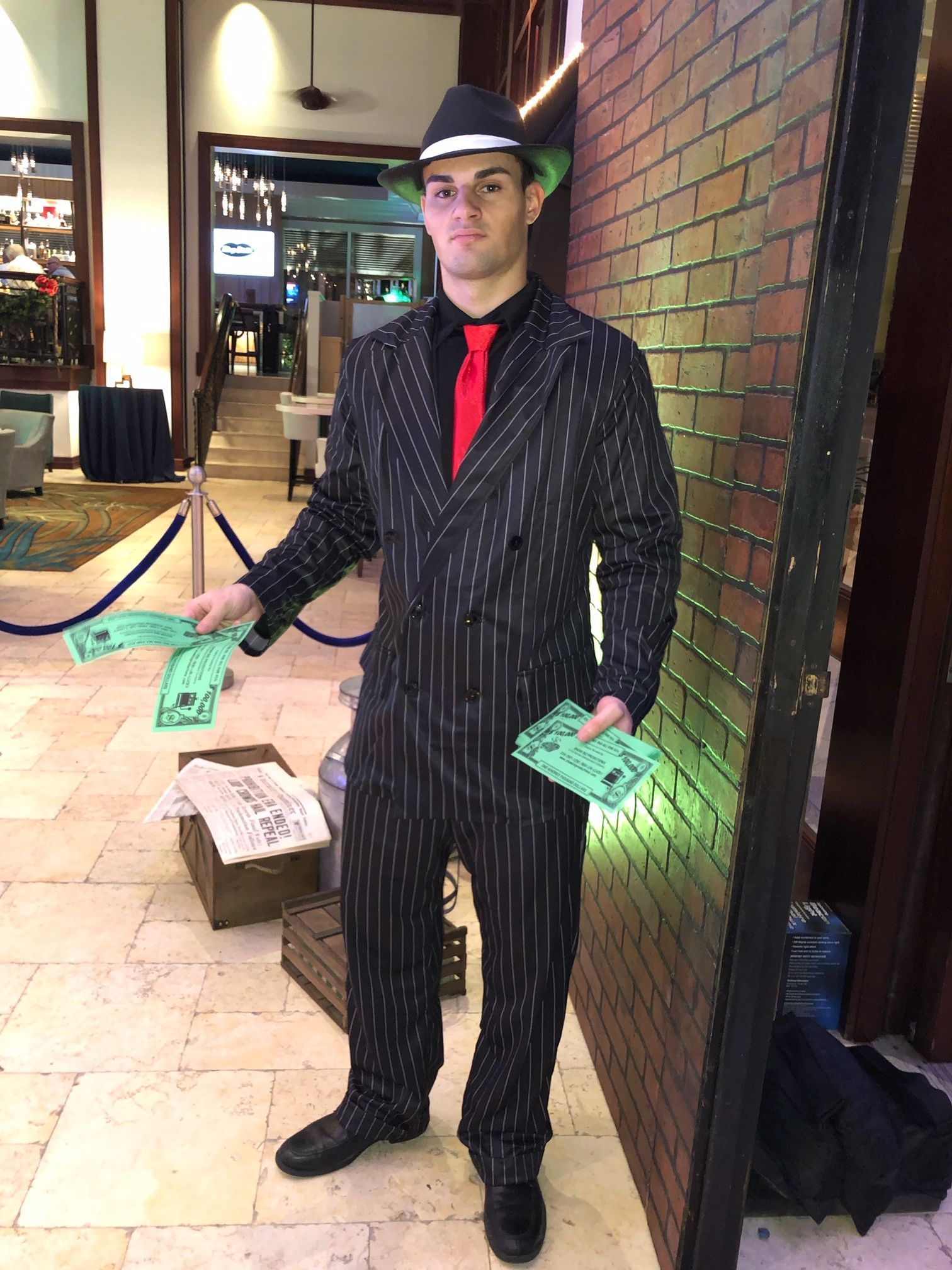 A man in a suit and hat is standing in front of a brick wall holding flyers.