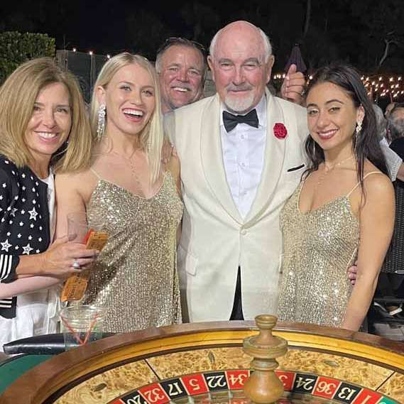 A group of people are posing for a picture in front of a roulette wheel.