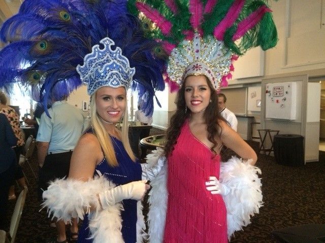 Two women are posing for a picture wearing feathered hats