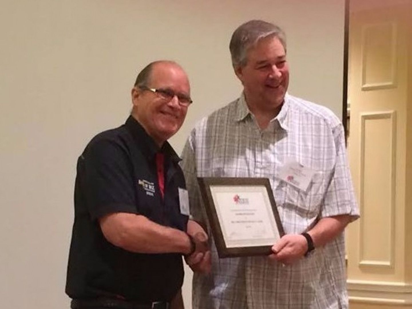 Two men are standing next to each other holding a framed certificate