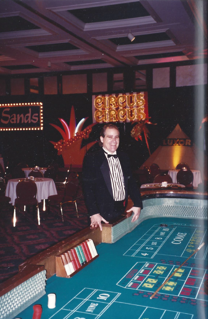 A man in a tuxedo stands in front of a roulette table in a casino