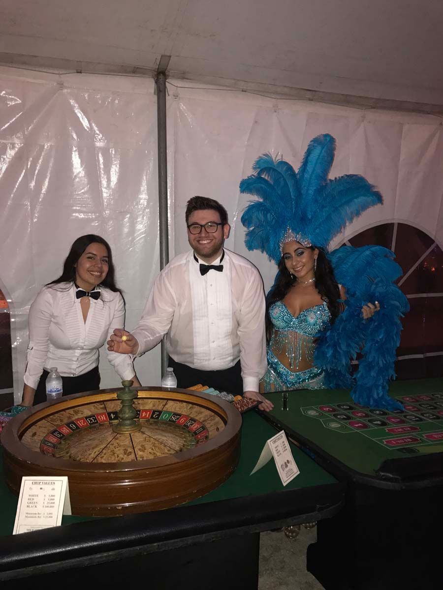 A man and two women are standing next to a roulette wheel.