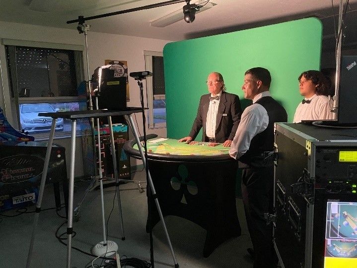 Three men are standing in front of a green screen in a room.