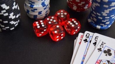 A stack of poker chips , dice , and playing cards on a table.