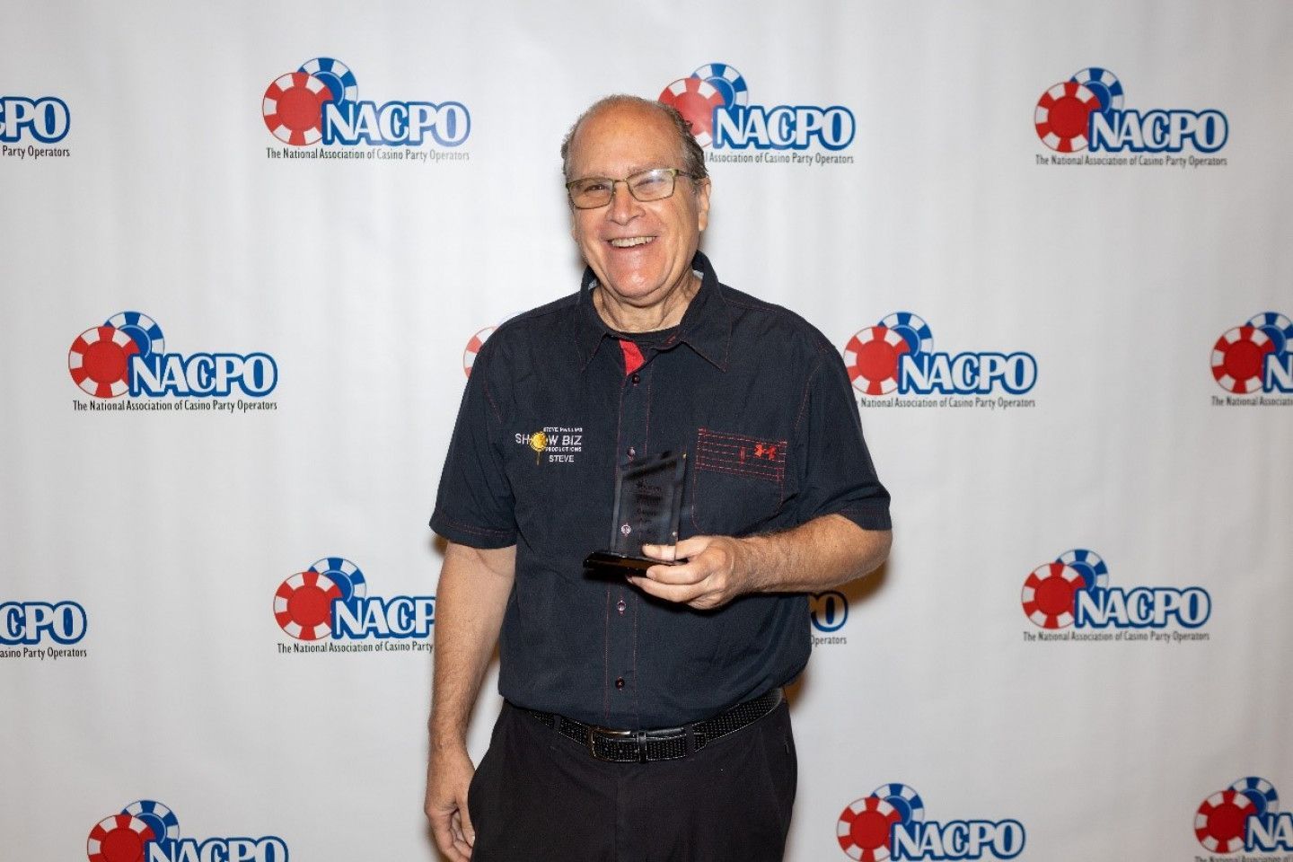 A man is holding a trophy in front of a nacpo backdrop.