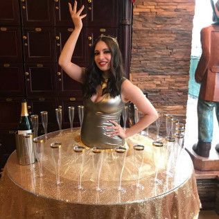A woman is standing in front of a table with champagne glasses and a bottle of champagne.