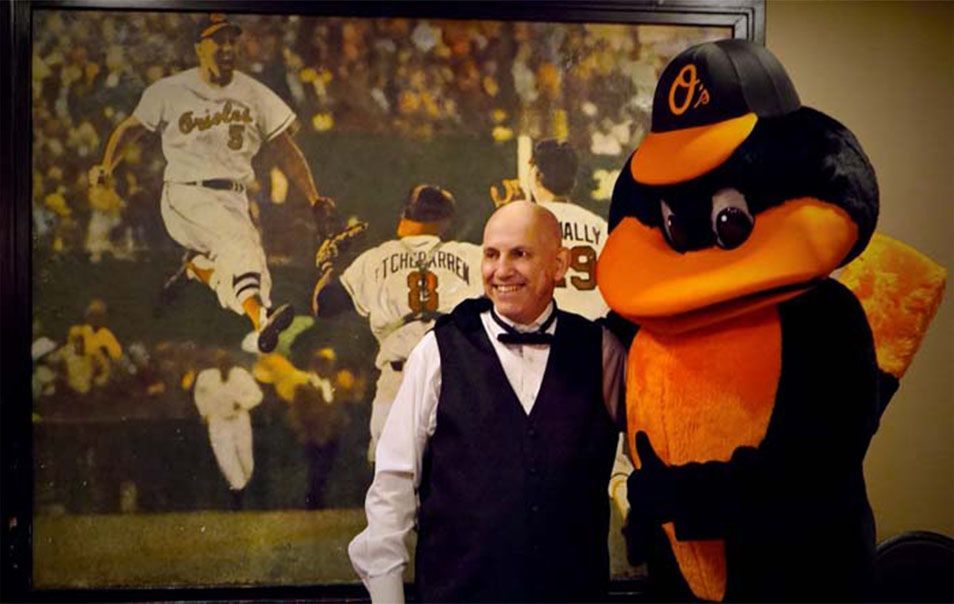 A man in a tuxedo stands next to an orioles mascot