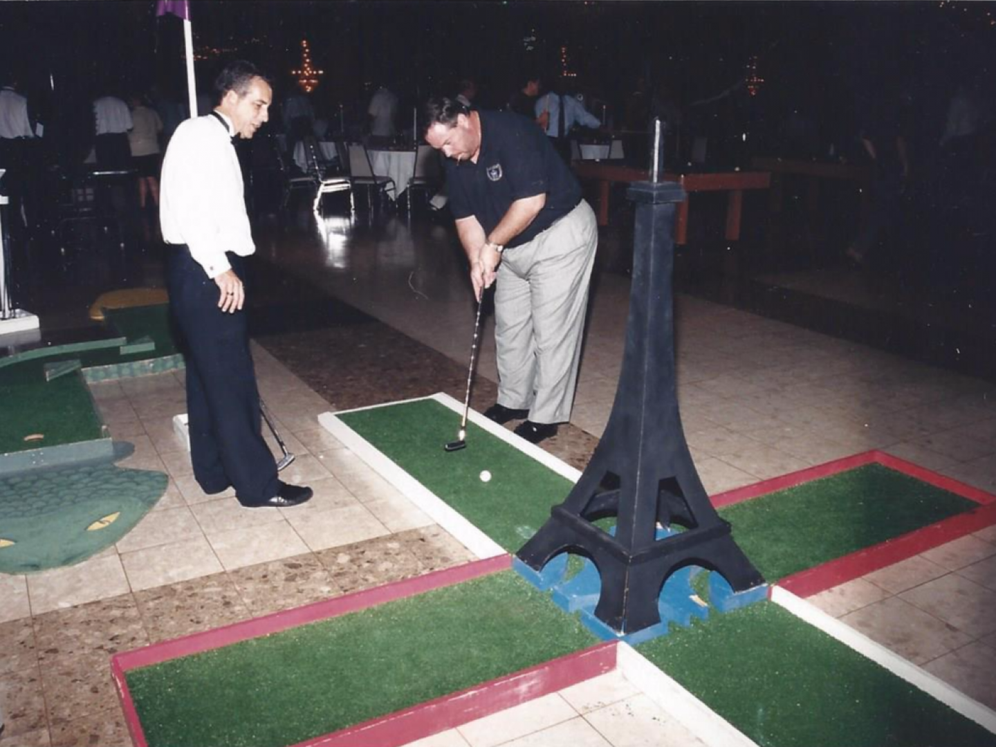 Two men are playing miniature golf in front of an eiffel tower