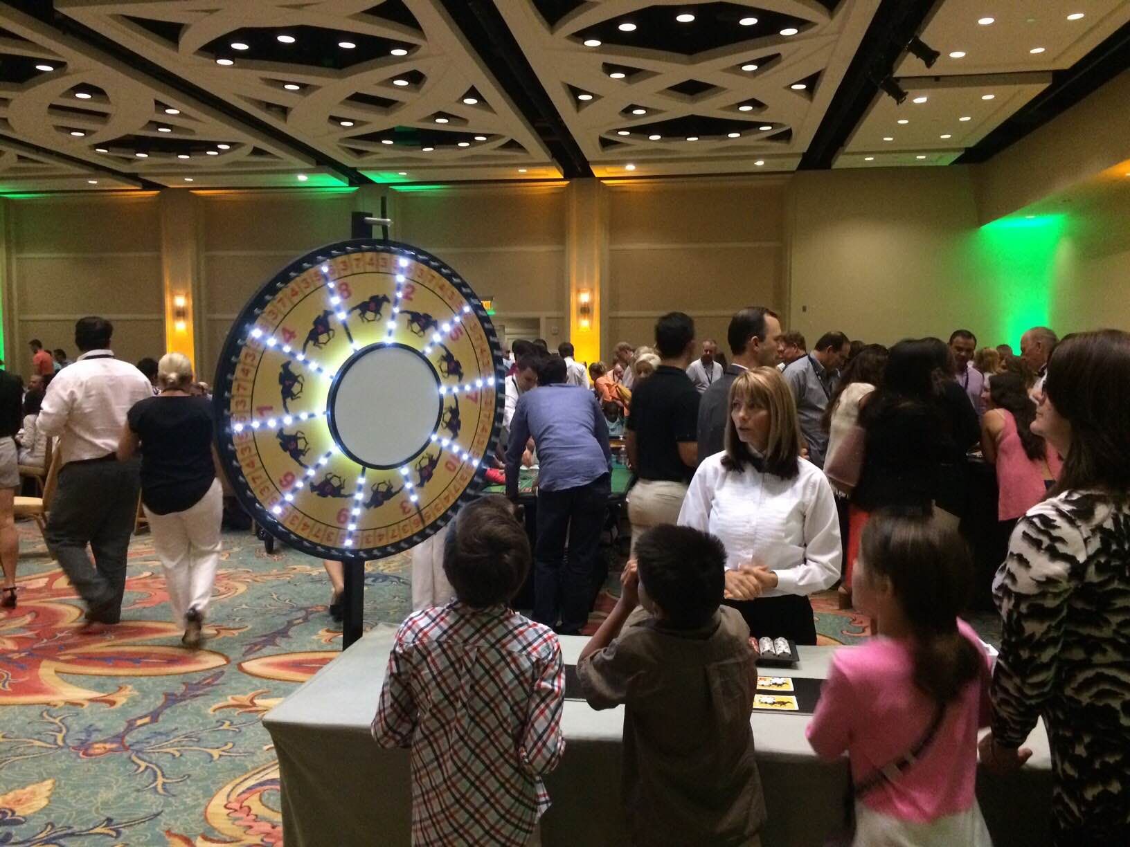 A group of people are standing around a wheel of fortune in a large room.