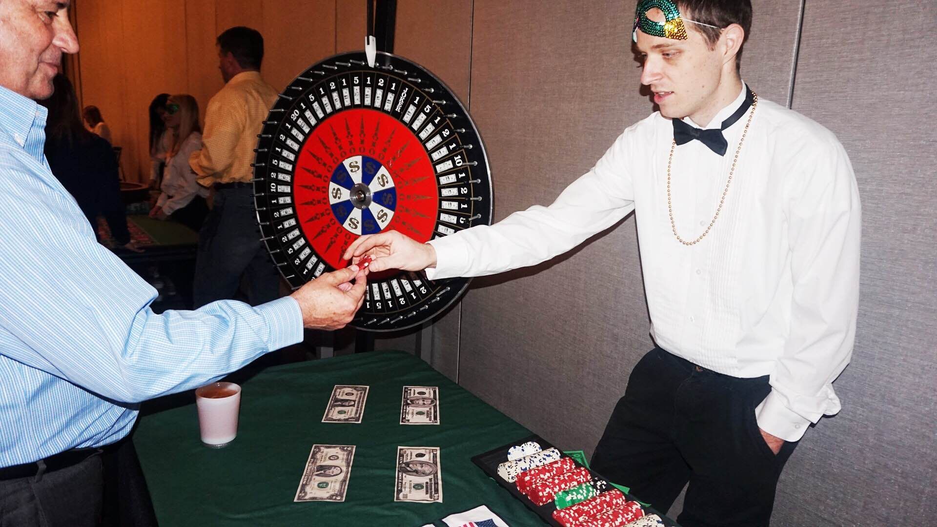 A man in a tuxedo is handing a roulette wheel to another man