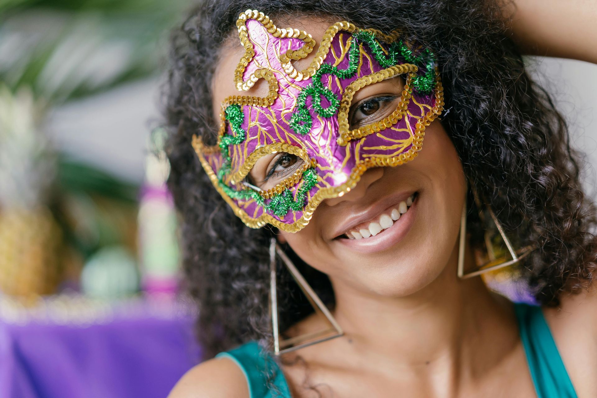 A woman wearing a carnival mask and earrings is smiling.