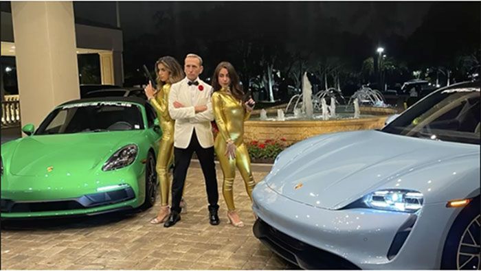 A man and two women are standing next to two porsche cars.