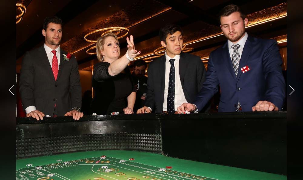 A group of people standing around a roulette table in a casino.