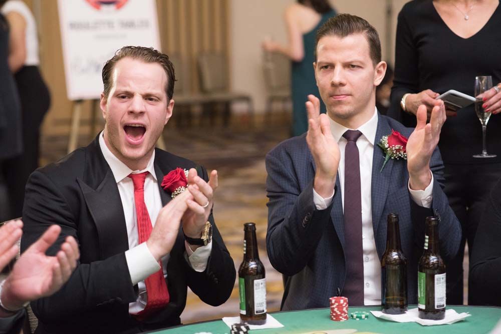 Two men in suits and ties are sitting at a table clapping their hands.