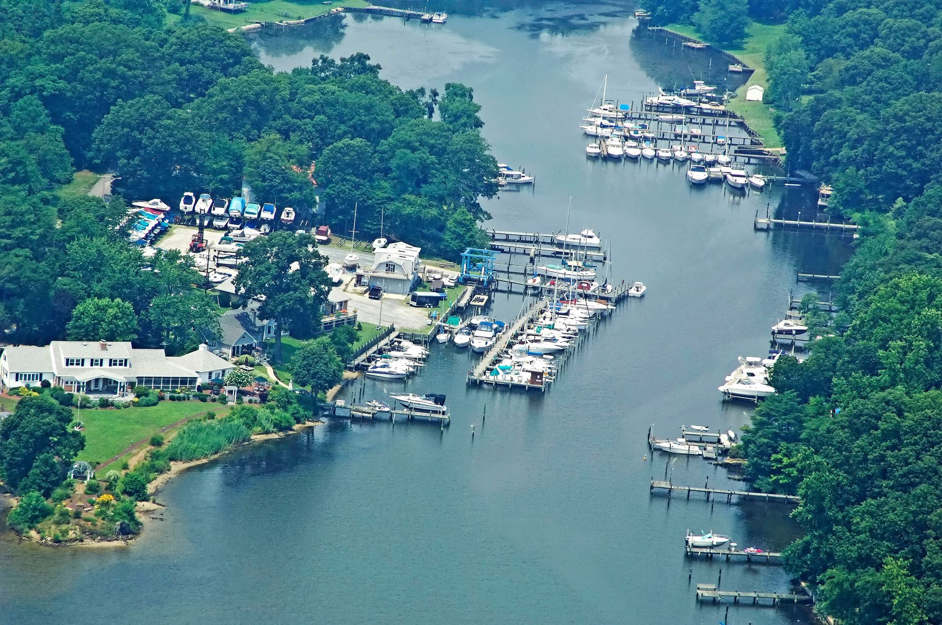 Aerial view of a marina with docks, boats, and green trees lining the water.