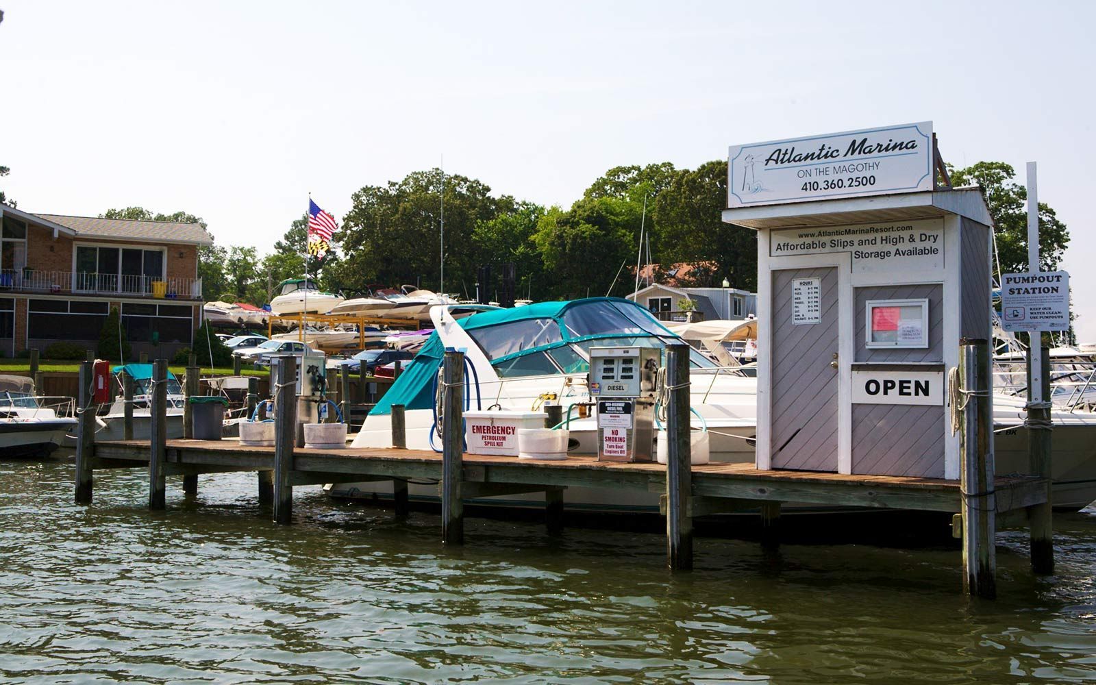 Dock with boats, a small marina building, and an open sign under a blue sky.