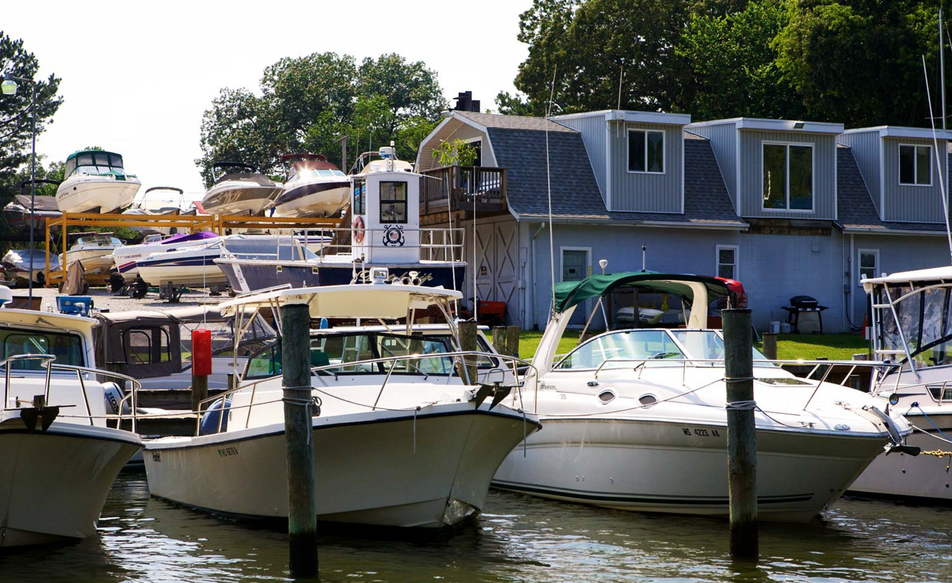 Boats docked at a marina; white motorboats in foreground, gray building with dormers in background.