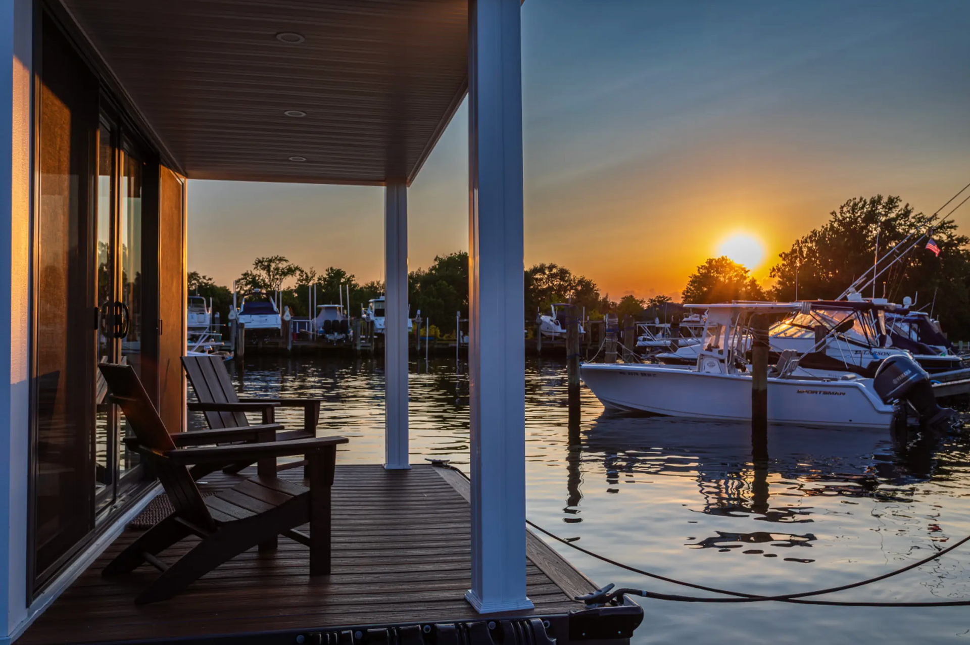 Sunset over a marina, boats moored. Wooden deck with chairs, view from a porch.