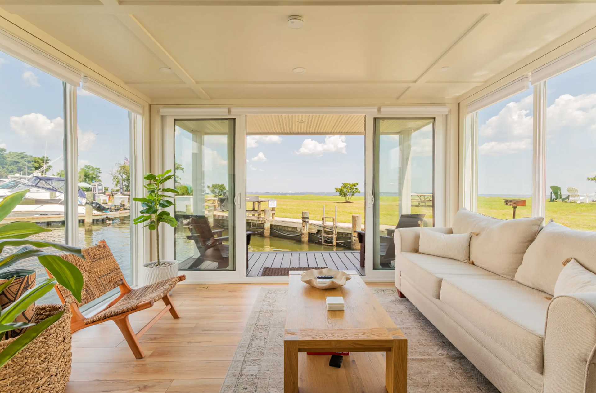 Living room with large windows overlooking water and dock. Includes couch, chair, coffee table, and plants.