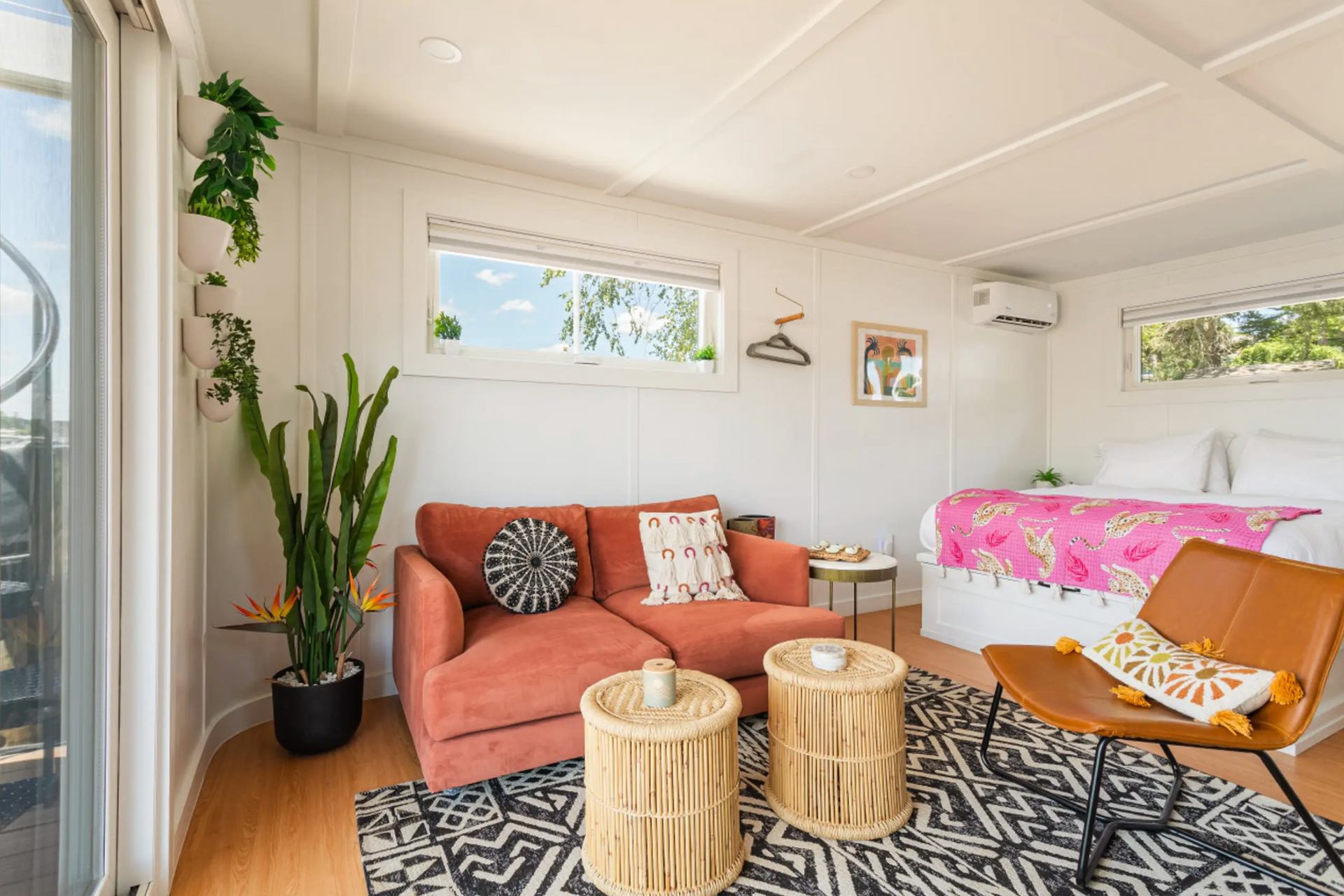 Bright, airy living space with orange couch, cactus, and bed with floral blanket.
