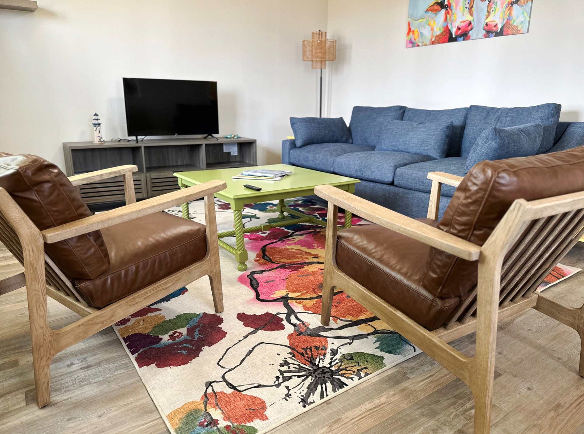 Living room with blue sofa, two brown leather chairs, green coffee table, and a colorful floral rug.