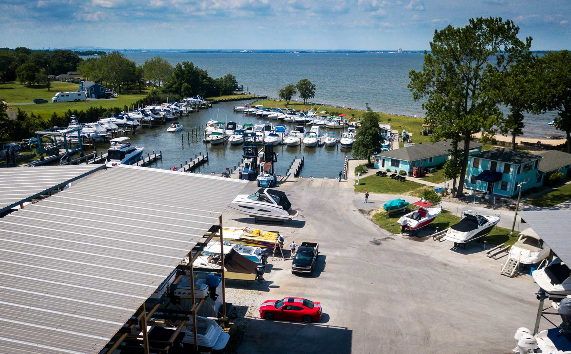Marina with boats docked, boat ramp, and water, under a sunny sky.