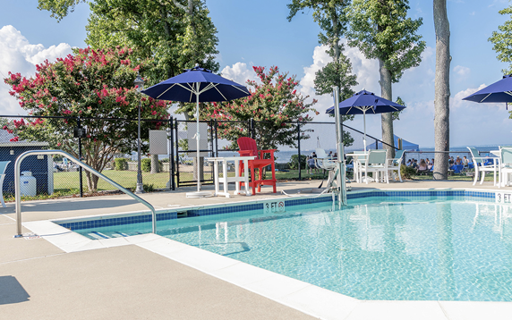 Swimming pool with blue umbrellas, a lifeguard chair, and trees on a sunny day.