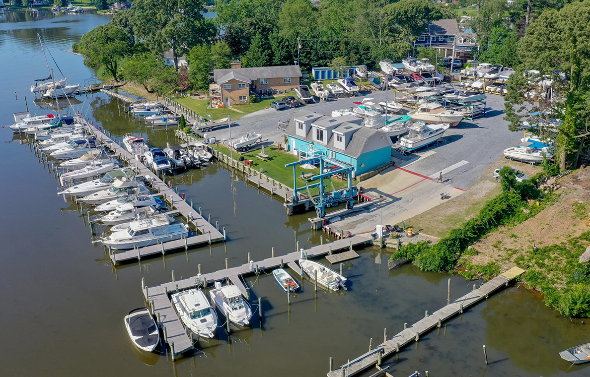 Aerial view of a marina with multiple docked boats, docks, a boat lift, and a blue building.