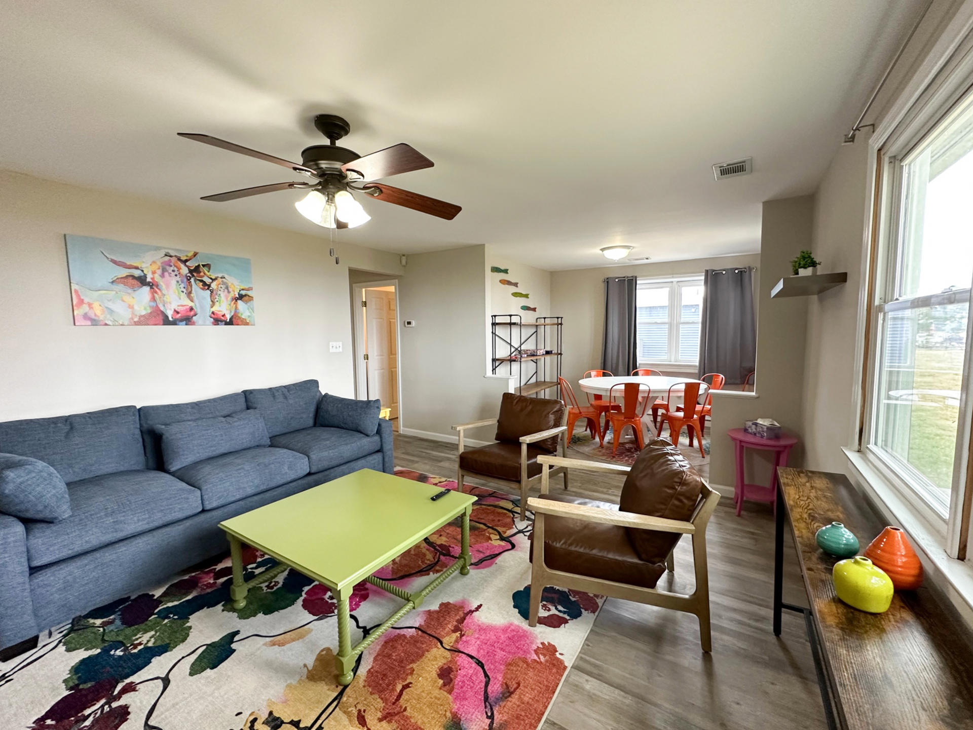 Living room with blue sofa, green coffee table, two brown chairs, and colorful rug.