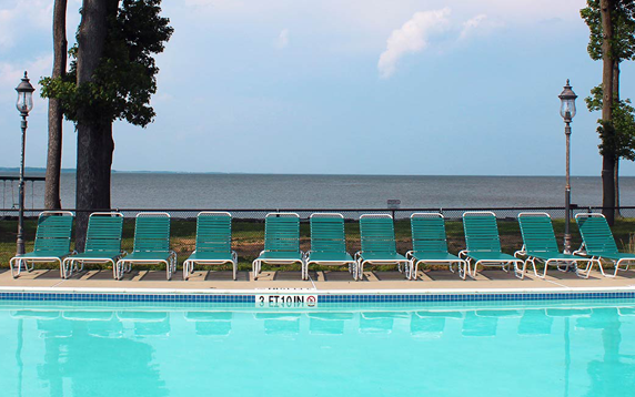 Swimming pool with rows of green lounge chairs facing a body of water under a blue sky.