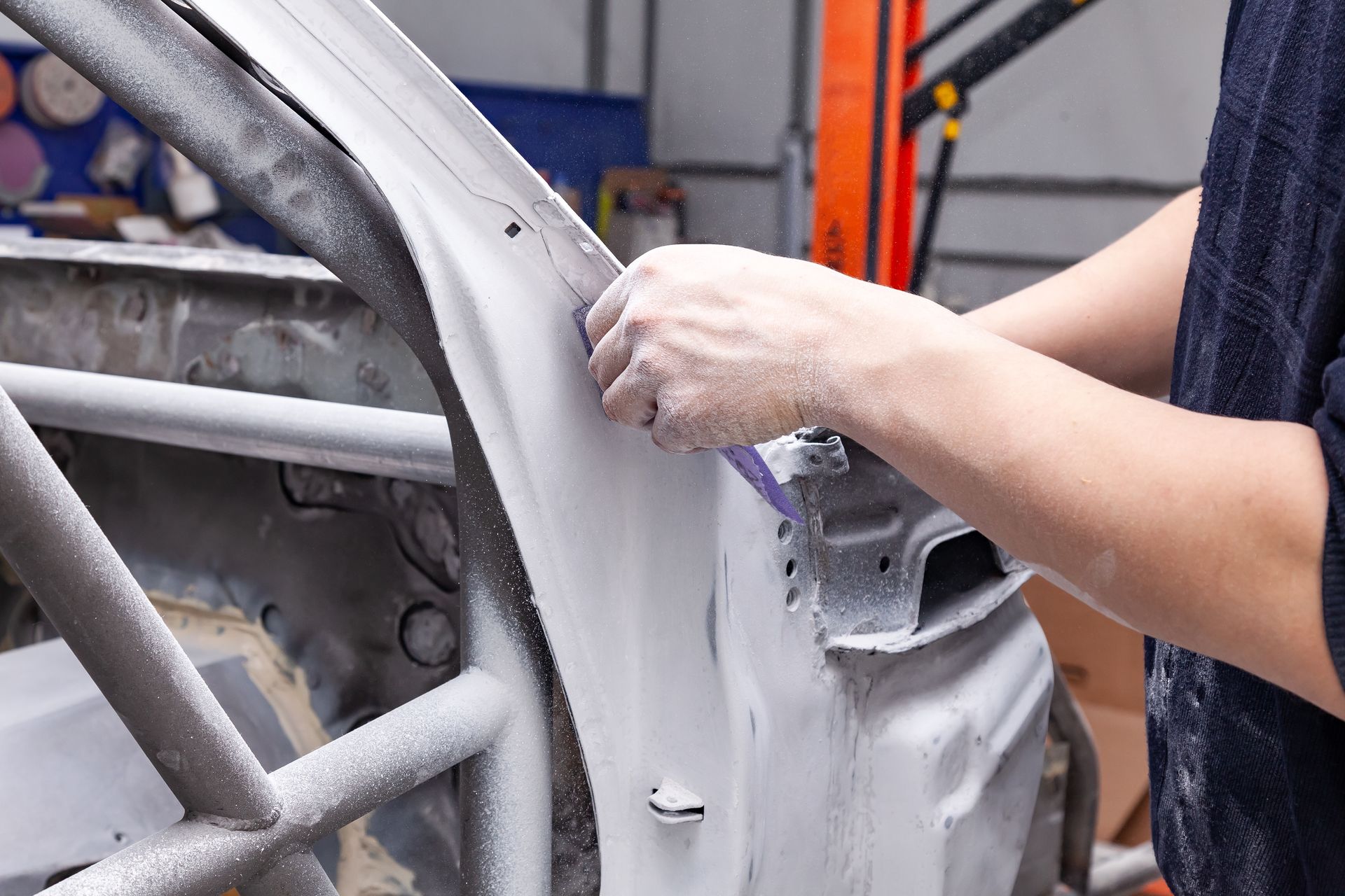 Mechanic in a red shirt inspecting a black car's hood in a workshop.