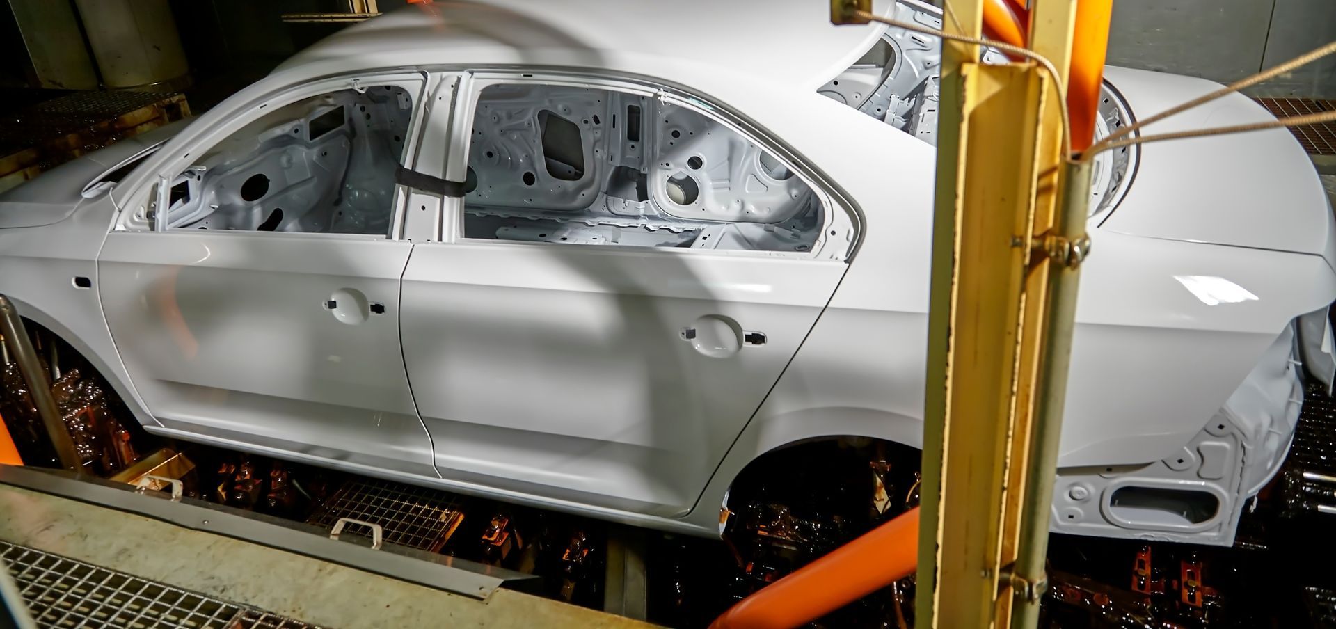A person uses a tool to fix a dent in a black car, lit by a fluorescent light in a workshop.