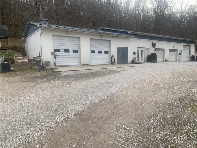 White commercial building with multiple garage doors and a gravel driveway in a wooded area.