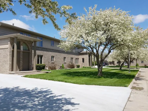 Building with brick facade, green lawn, blooming white trees, and blue sky.