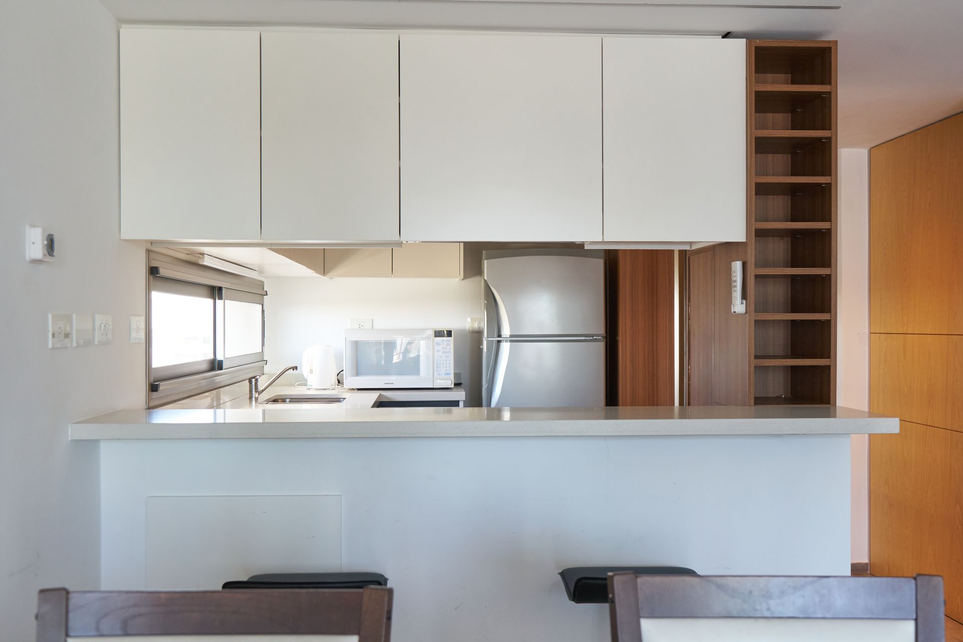 Cocina moderna con gabinetes blancos, refrigerador de acero inoxidable y barra de desayuno.