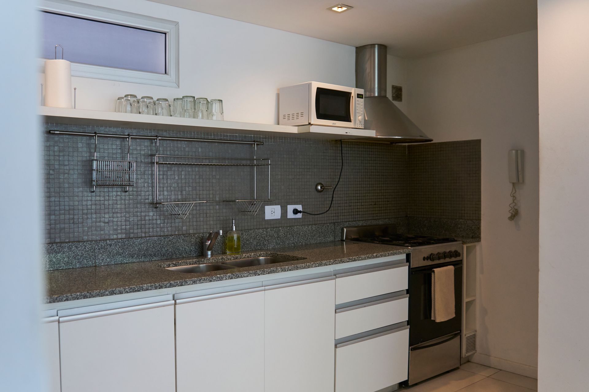 Cocina pequeña y moderna con gabinetes blancos, electrodomésticos de acero inoxidable y protector contra salpicaduras gris.