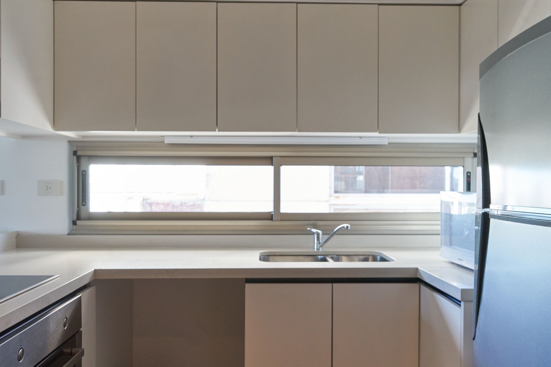 Cocina moderna con gabinetes neutrales, electrodomésticos de acero inoxidable y una ventana sobre el fregadero.