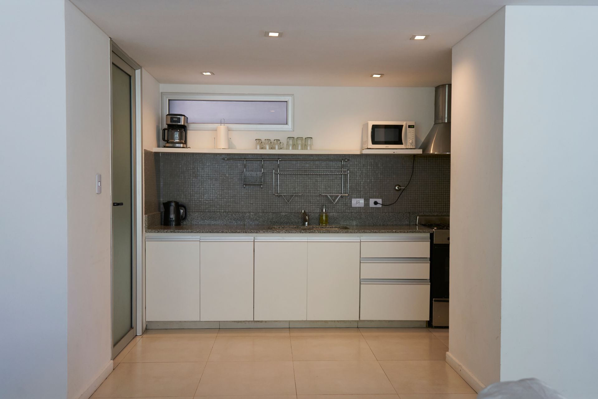 Pequeña cocina moderna con gabinetes blancos, salpicadero de granito y electrodomésticos.