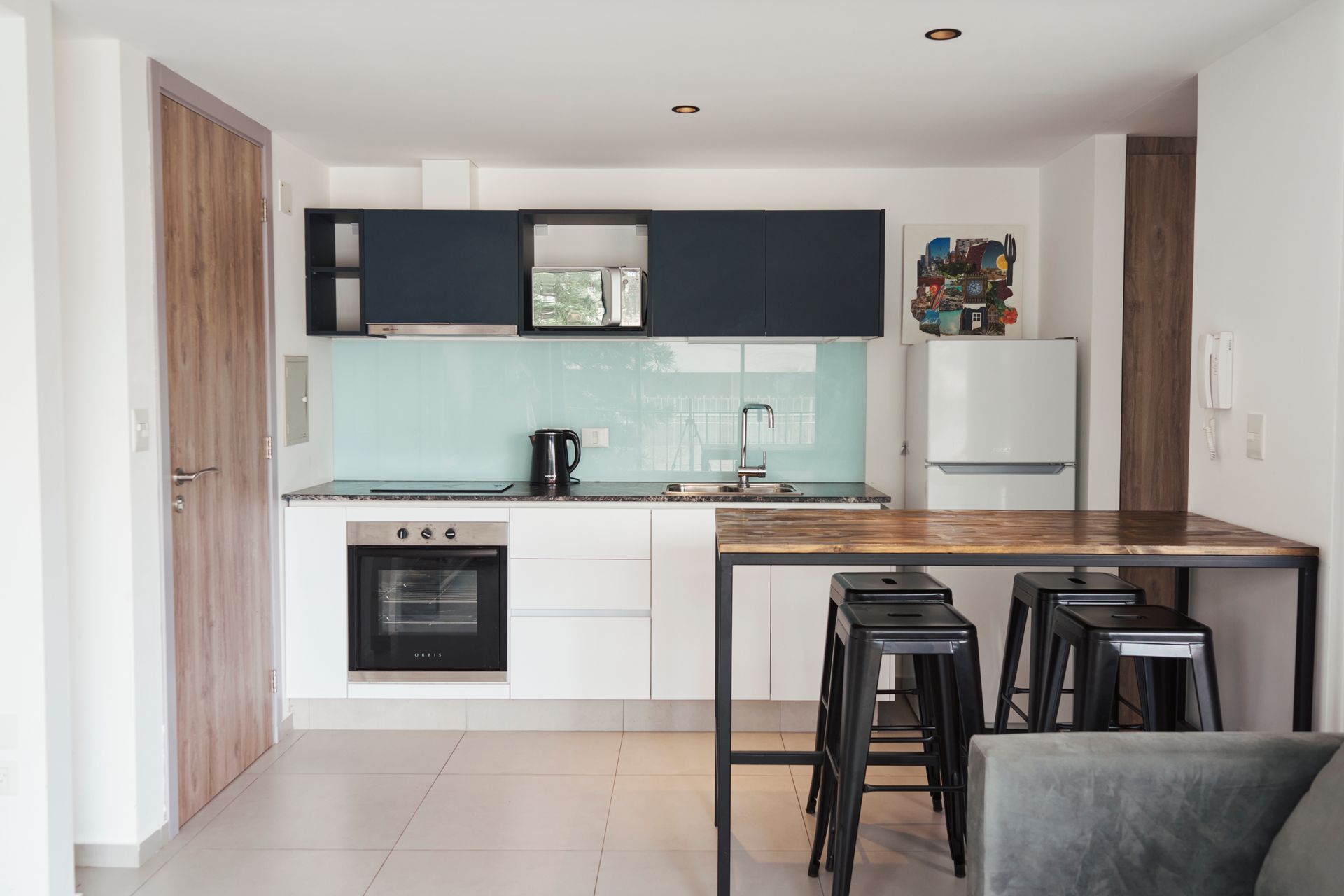 Cocina moderna con gabinetes blancos, protector contra salpicaduras azul y asientos de barra.